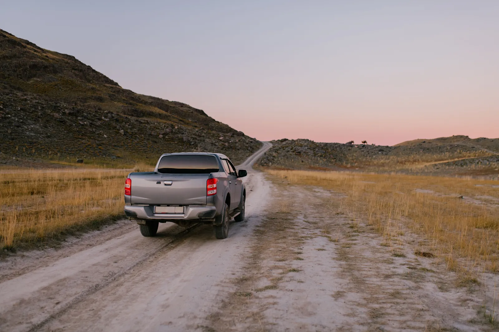 Pickup truck traveling down a dusty rural road at sunset