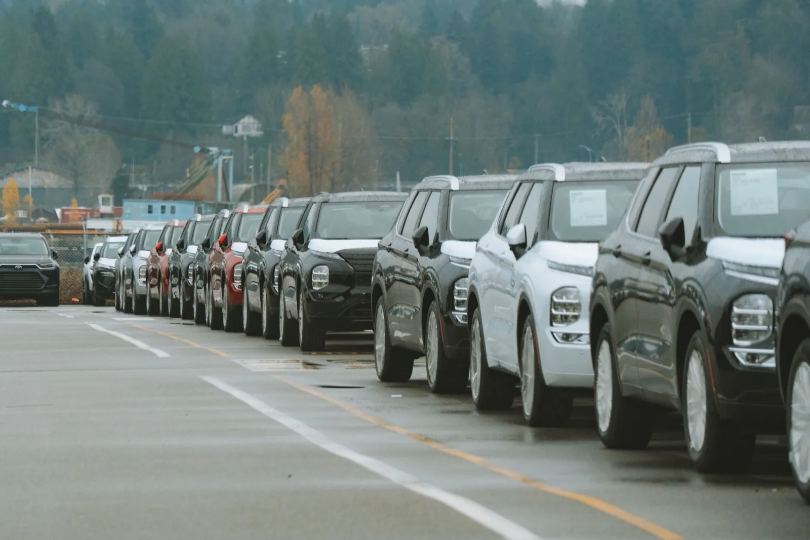 New cars parked in a row on a dealership lot on an overcast day