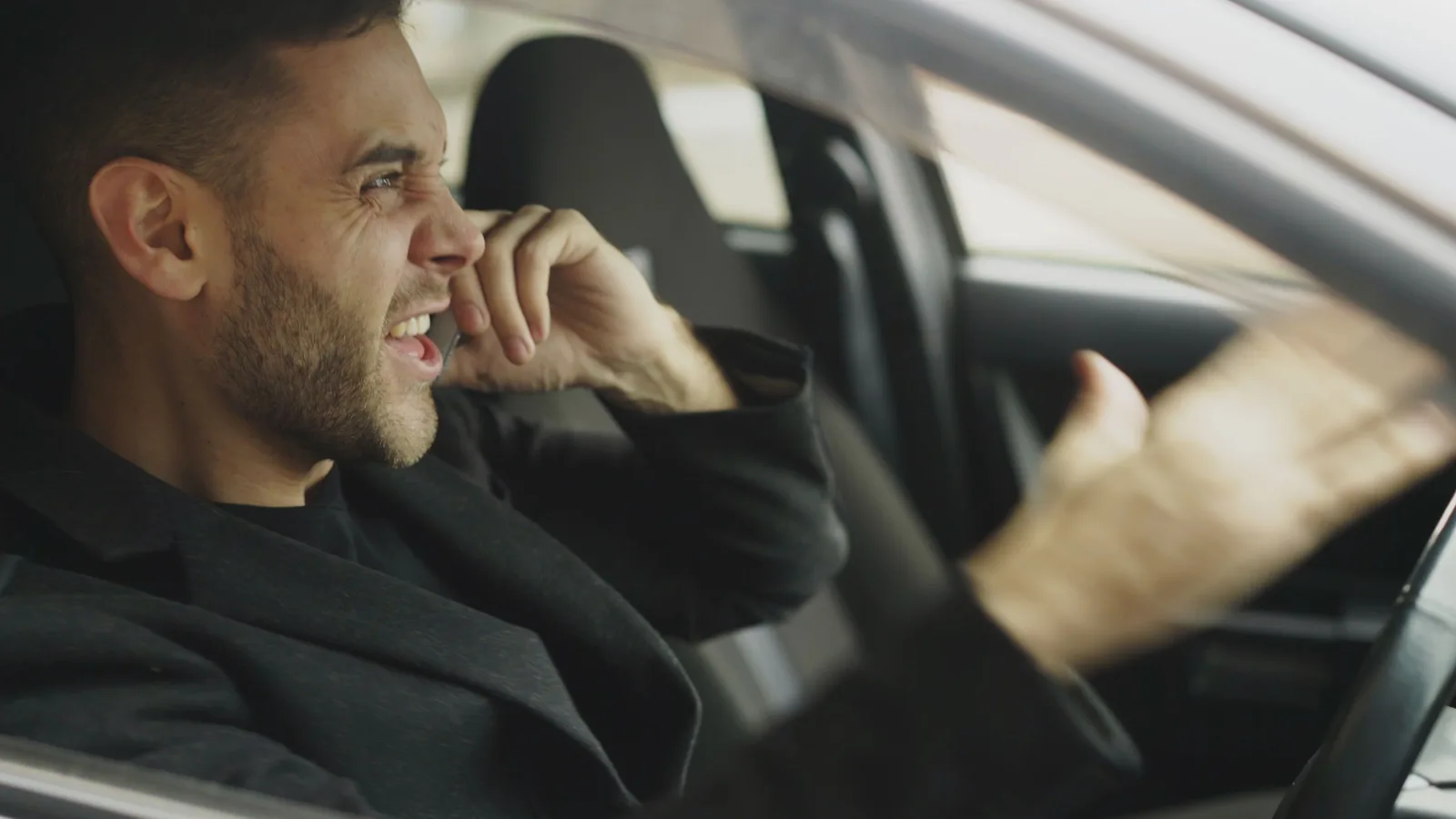 Man on a phone call inside a parked car, looking frustrated