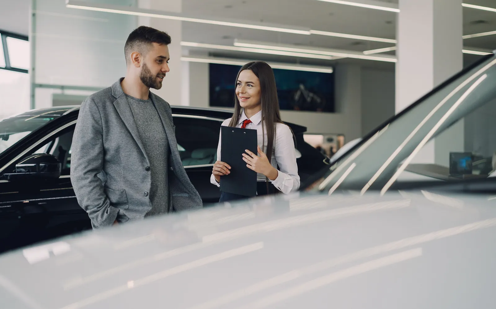 A car shopper talking with a salesperson holding a clipboard in a dealership showroom