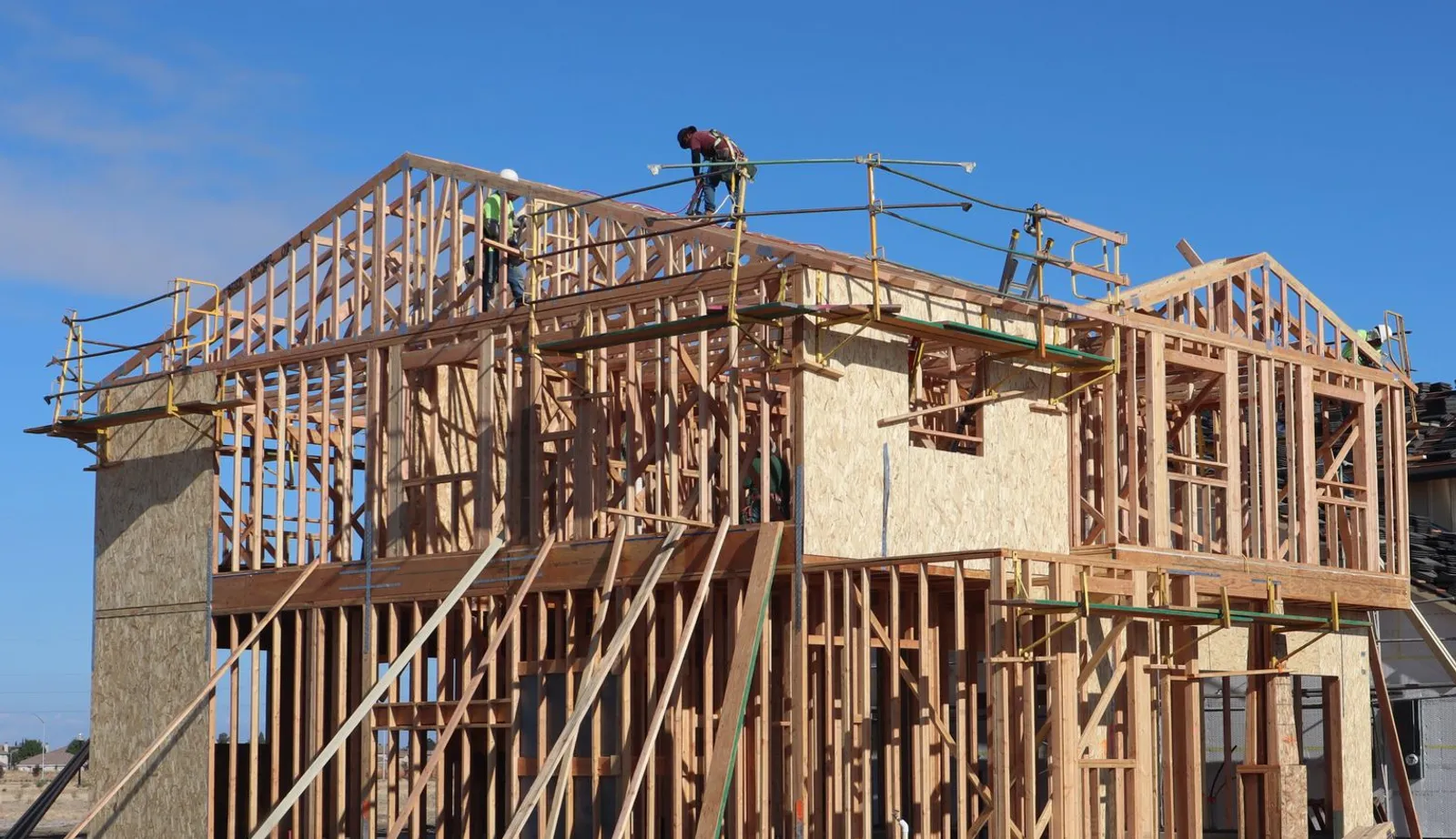 Workers framing a two-story wood house under a clear blue sky