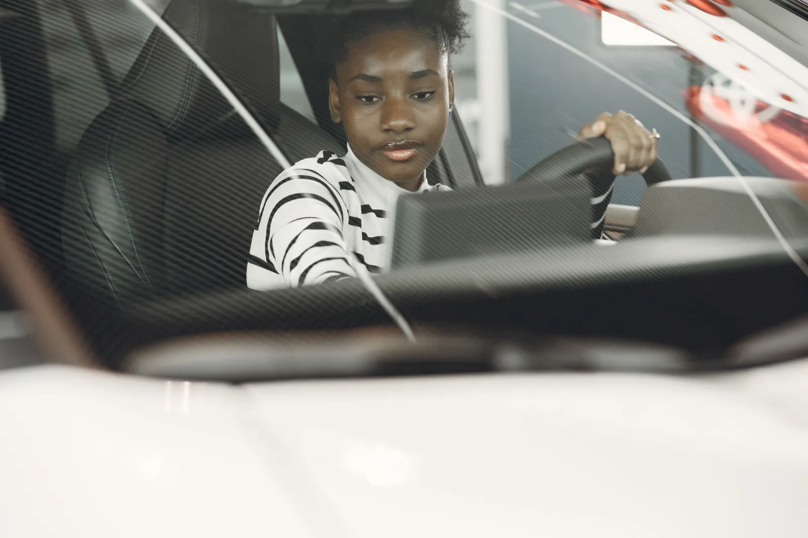 A woman alone in the driver seat with both hands on the steering wheel, seen through the windshield