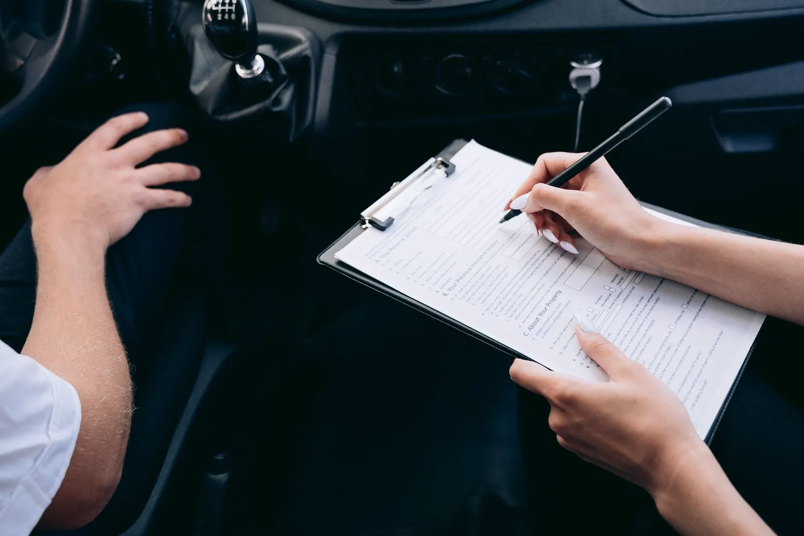 Two people filling out a finance form on a clipboard in the front seat of a car