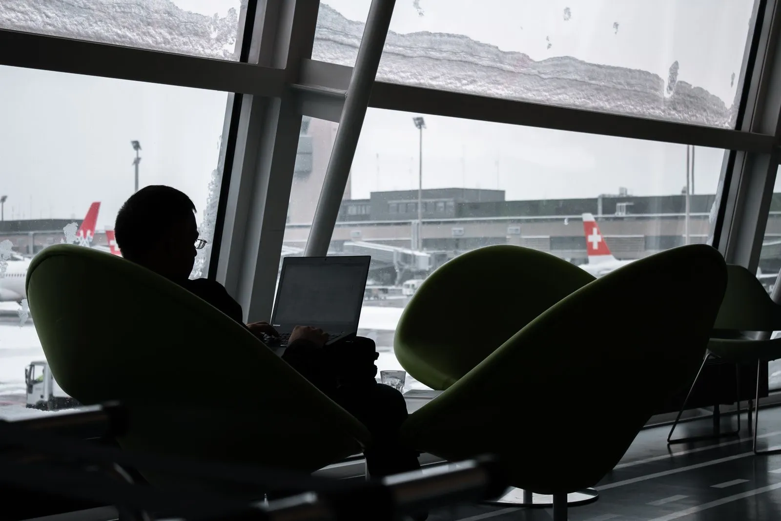 Silhouette of a traveler working on a laptop in an airport lounge with planes outside the window