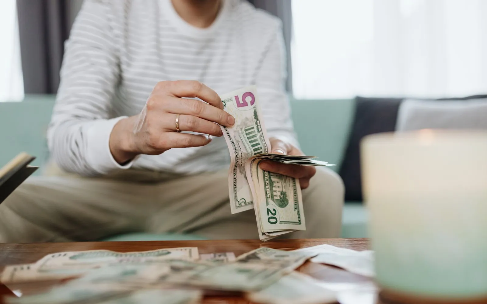 Person on a couch counting five and twenty dollar bills over a coffee table