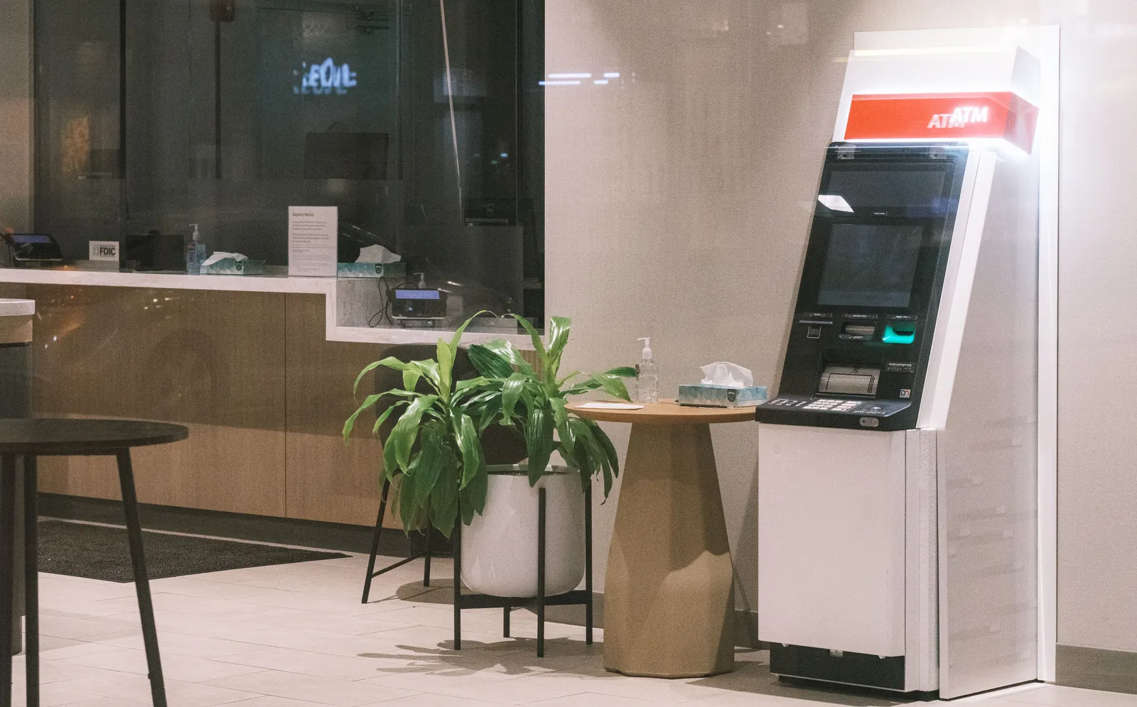 An empty ATM beside a potted plant in a quiet bank lobby