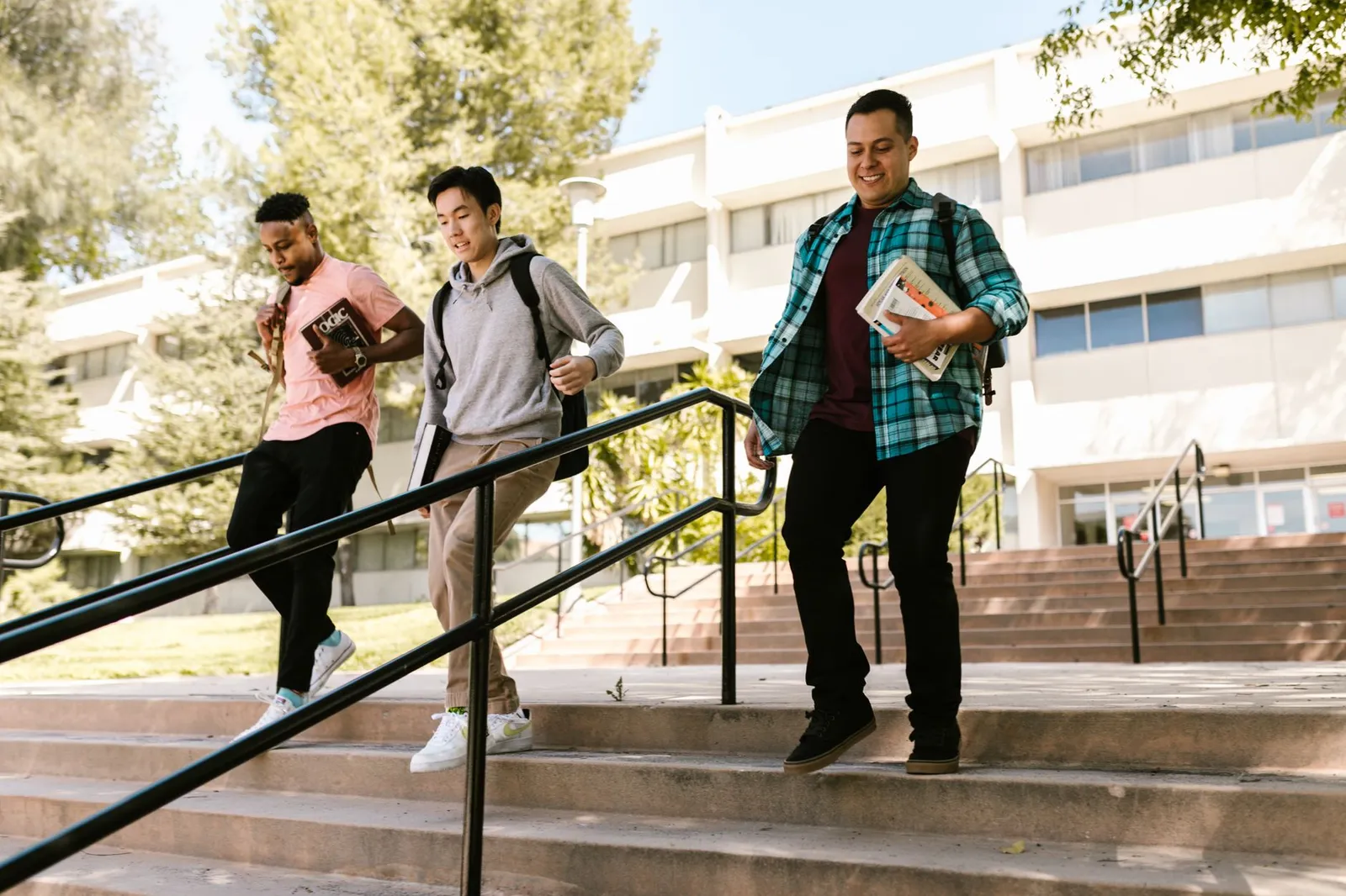 Three college students carrying books walking down steps outside a campus building