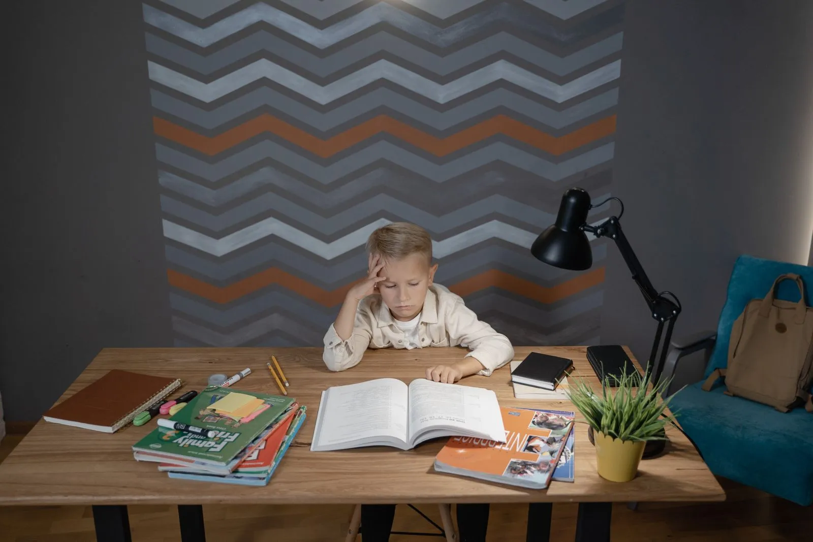 A student writing at a school desk with a stack of books in soft daylight