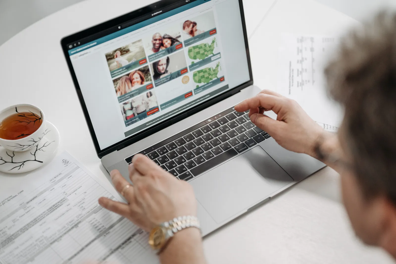 Person searching on a laptop at a desk with documents and a cup of tea beside them