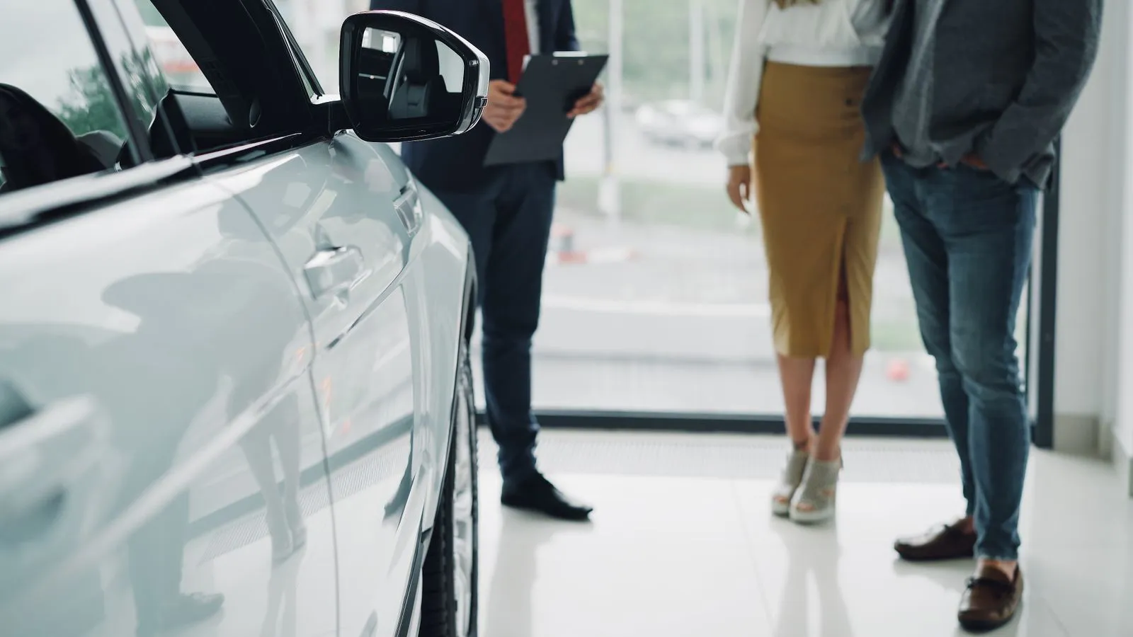 Car buyer and dealership staff going over paperwork at a desk in a showroom