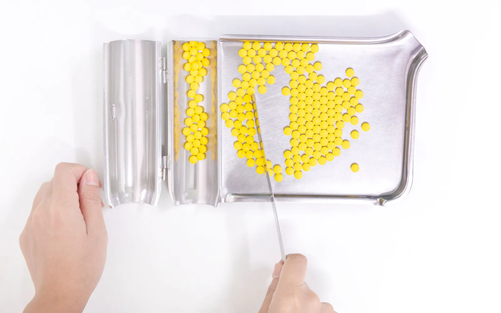 Hands counting yellow tablets on a stainless steel pharmacy counting tray