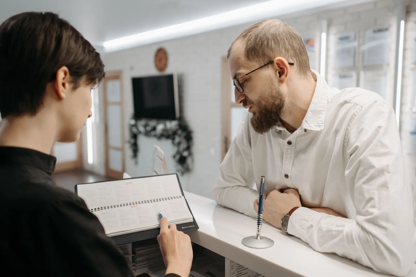A receptionist showing an appointment planner to a man at a clinic front desk