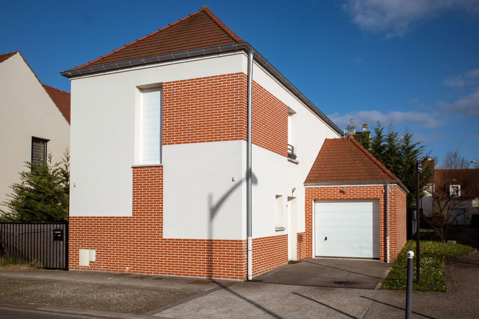 Modern suburban house with a red brick and white facade in a sunny neighborhood