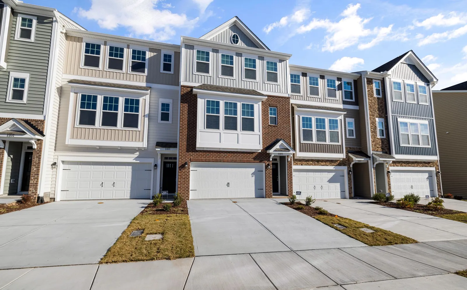 A row of modern suburban townhouses with driveways under a blue sky