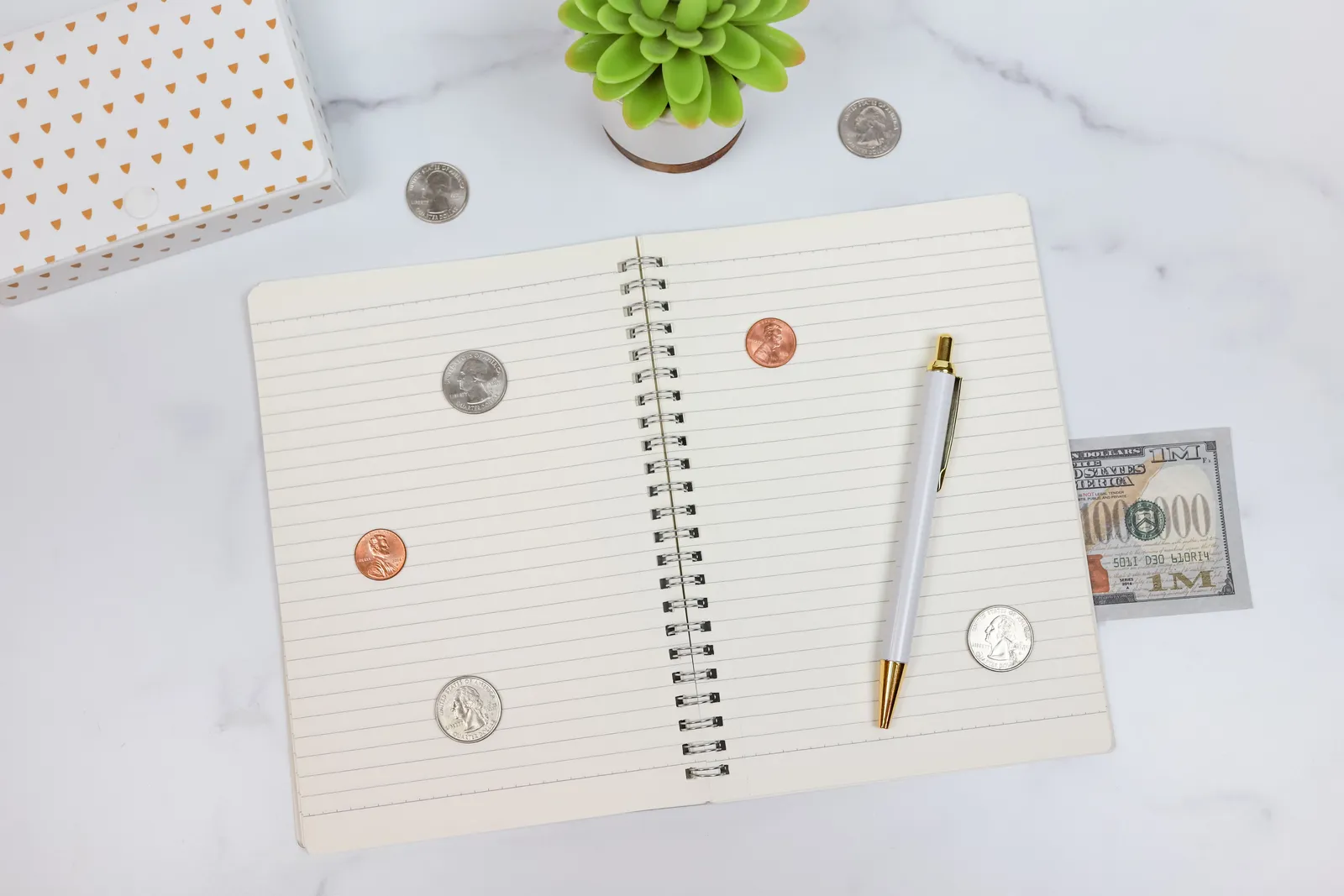 US currency, an open notebook, and a pen on a marble desk