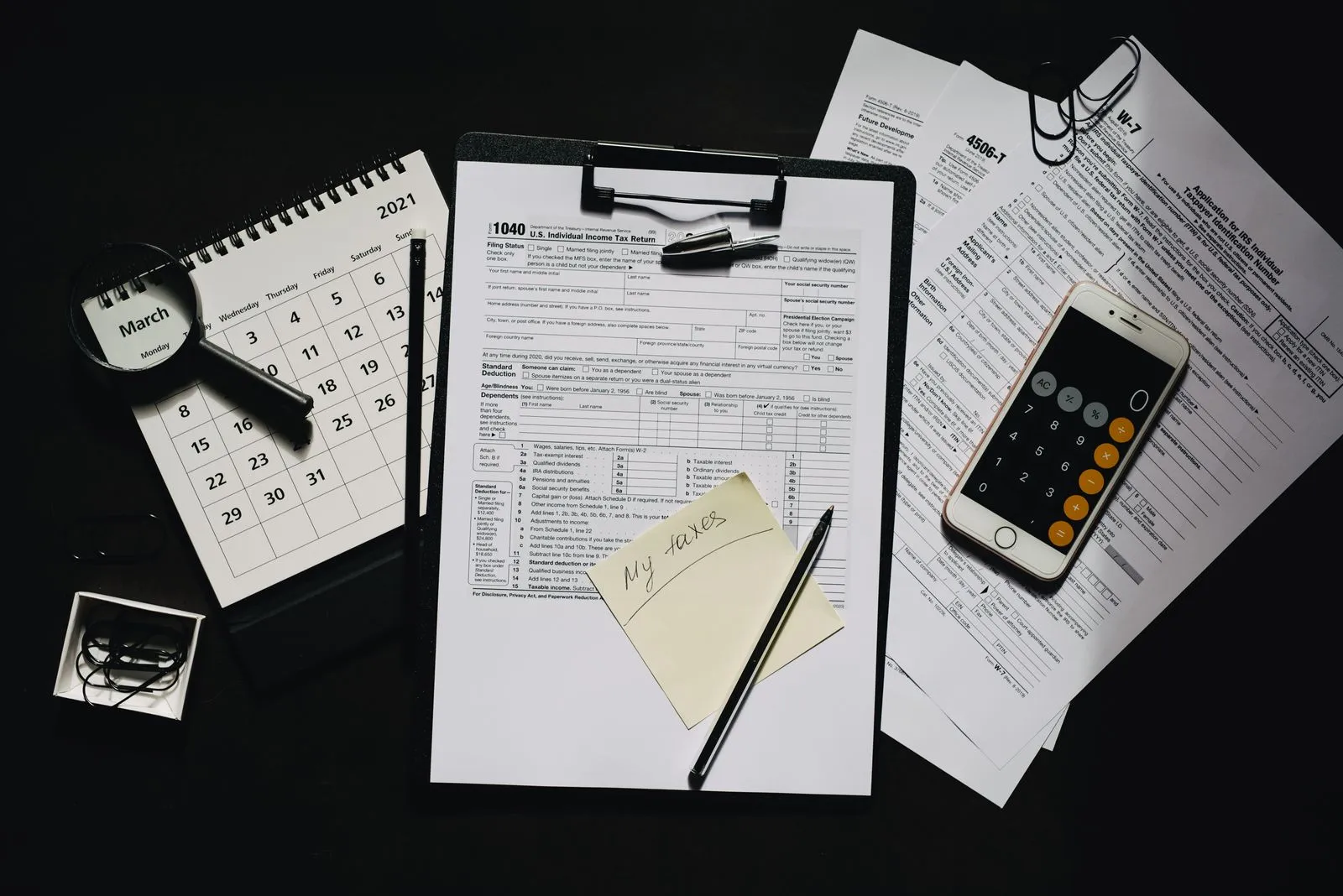 Tax forms and a calculator laid out on a wooden desk with a pen