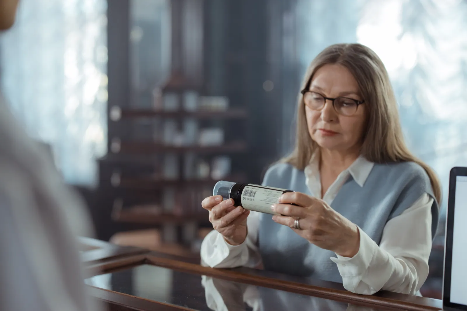 Adult woman inspecting a prescription medicine bottle in a pharmacy.