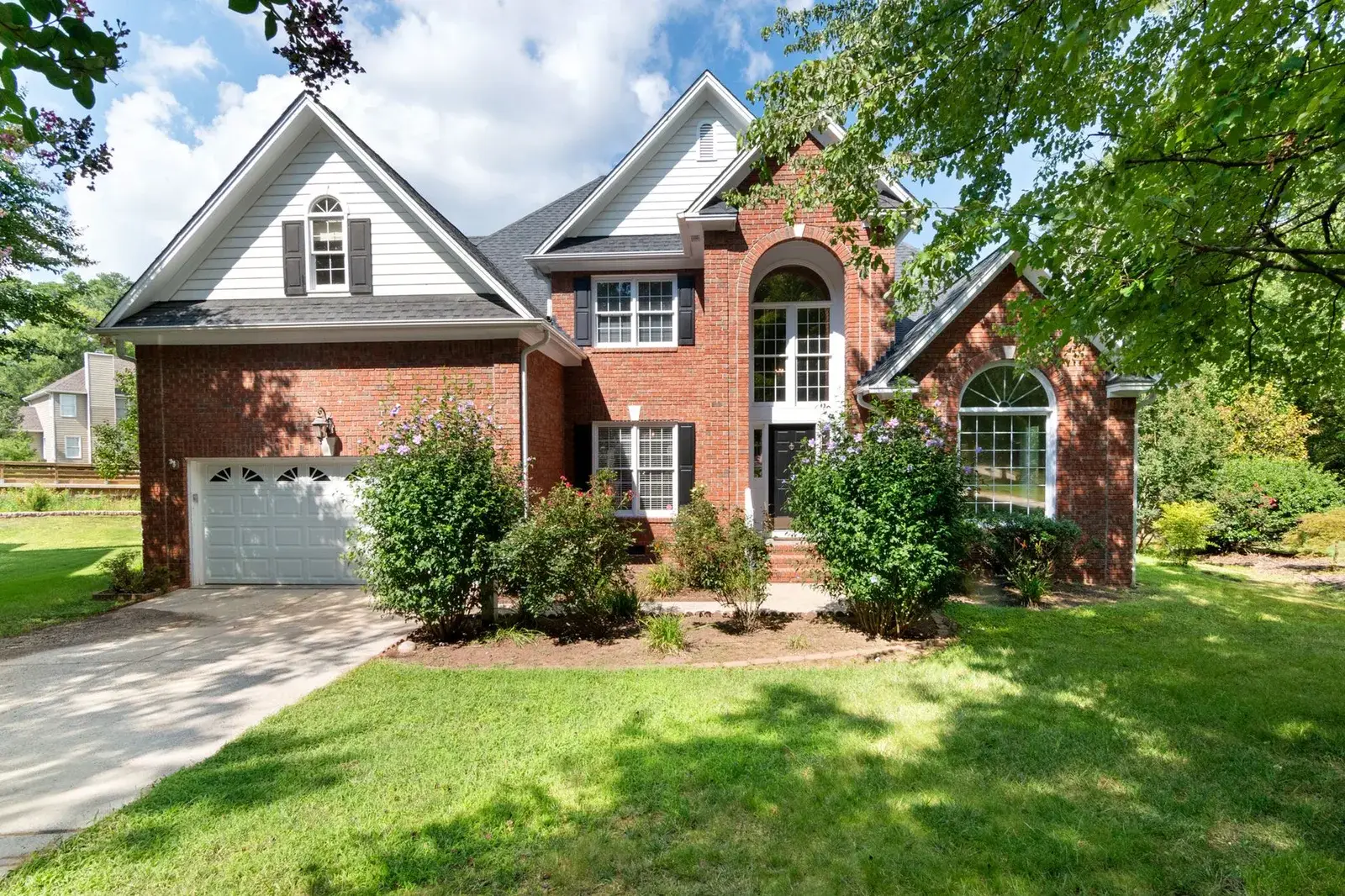 Two-story brick house with a garage and a front lawn on a sunny day