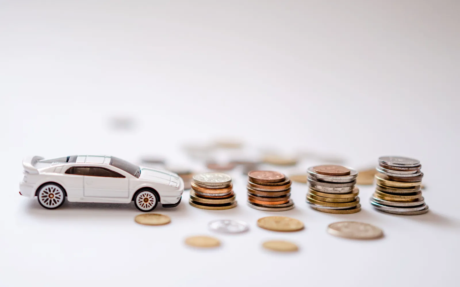 A white toy car parked beside stacks of coins that grow taller from left to right