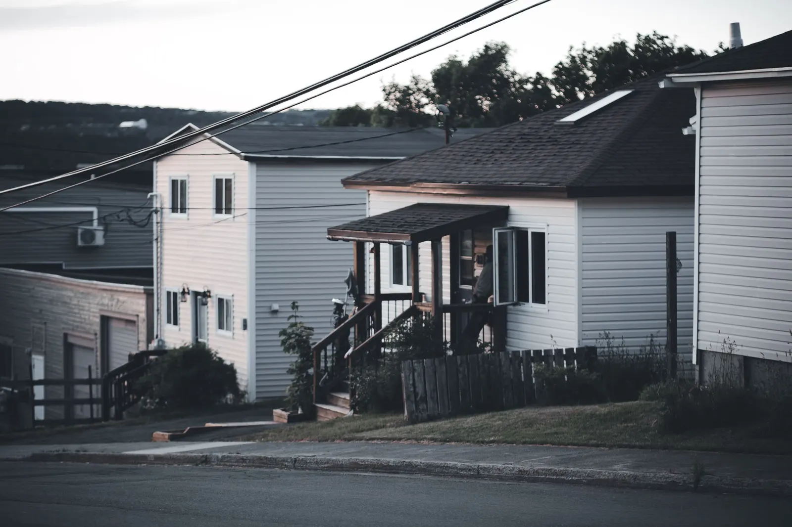 Power lines running past sided houses on a quiet residential street at dusk