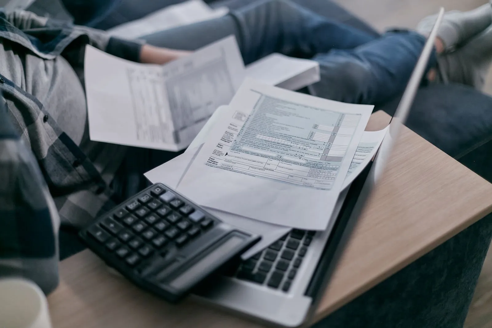 A person at a kitchen table using a calculator and laptop to work through loan paperwork
