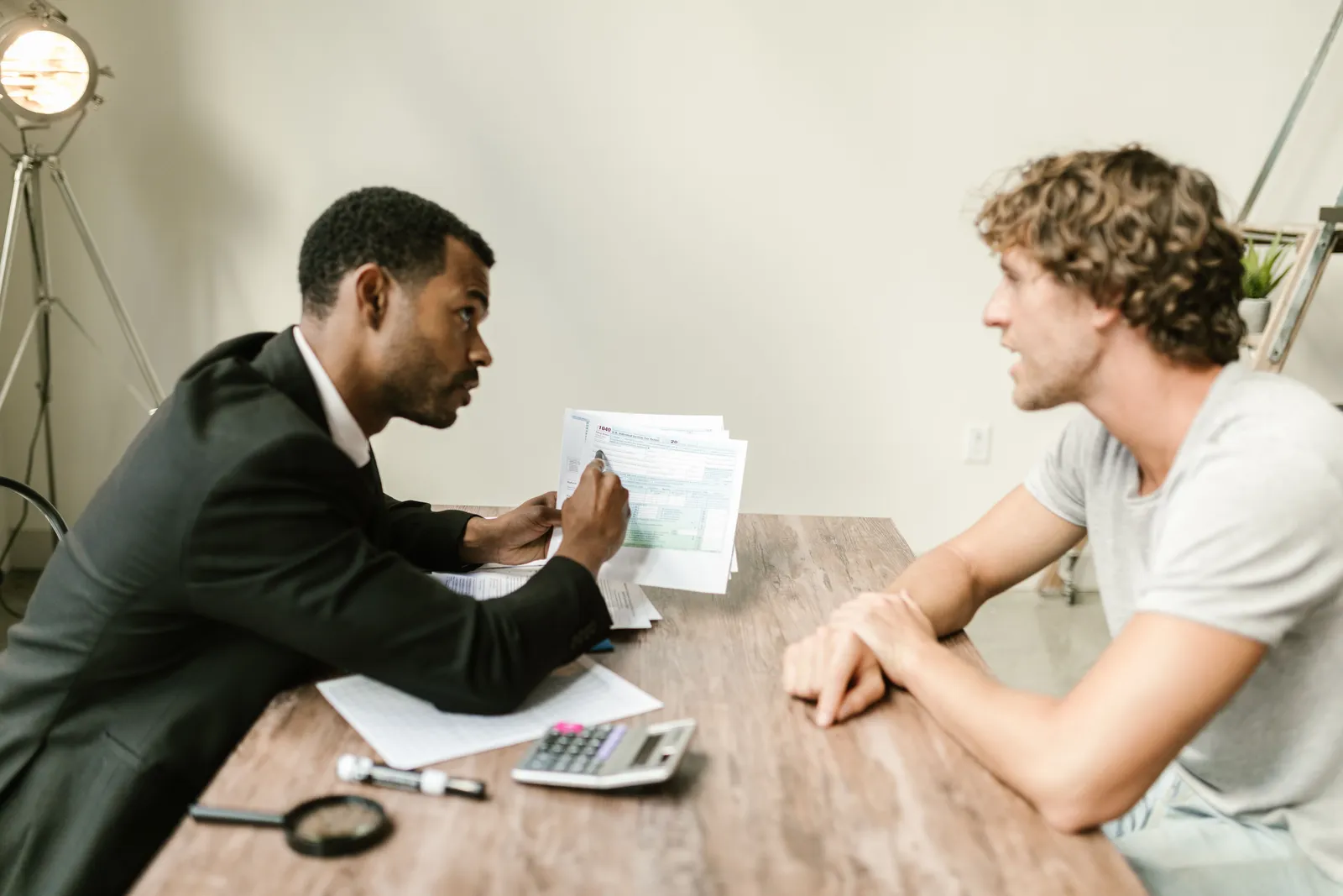Two people reviewing printed financial paperwork across a wooden desk with a calculator