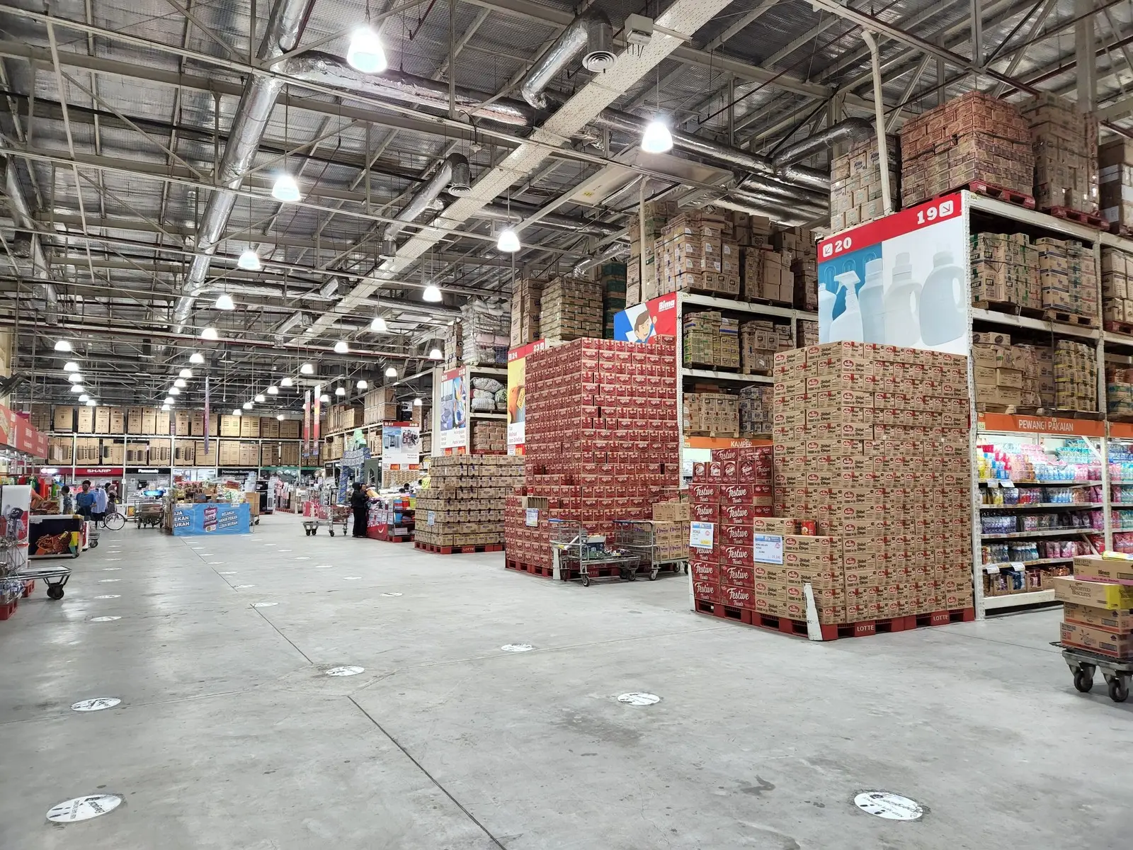Shopper pushing a full flatbed cart through a warehouse club aisle