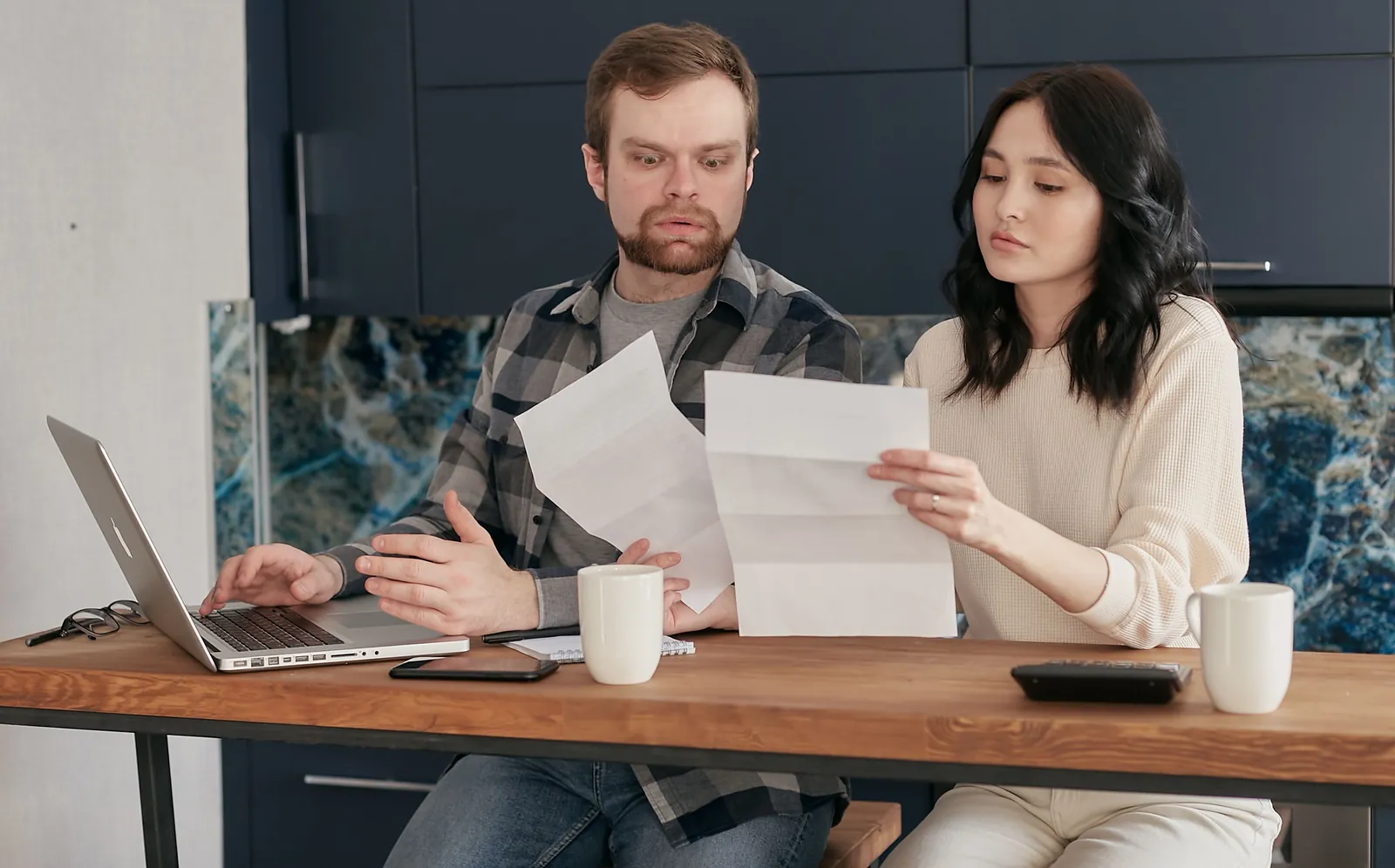 A couple reading loan statements at a kitchen table with a laptop and coffee