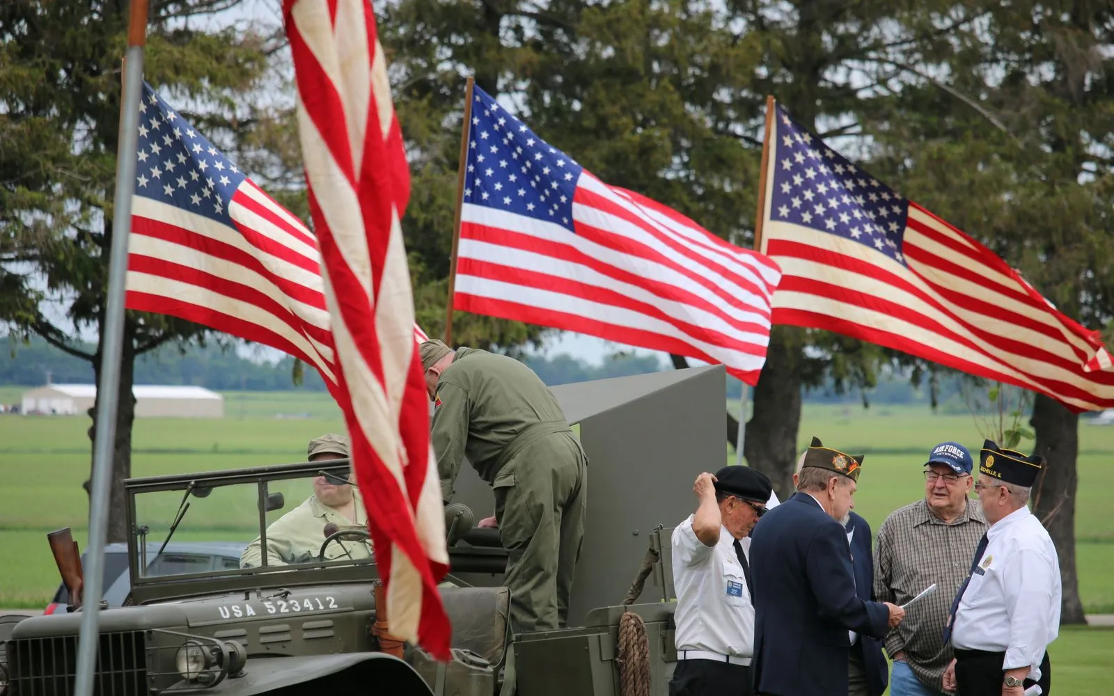 Service members in uniform standing beside a military vehicle with American flags