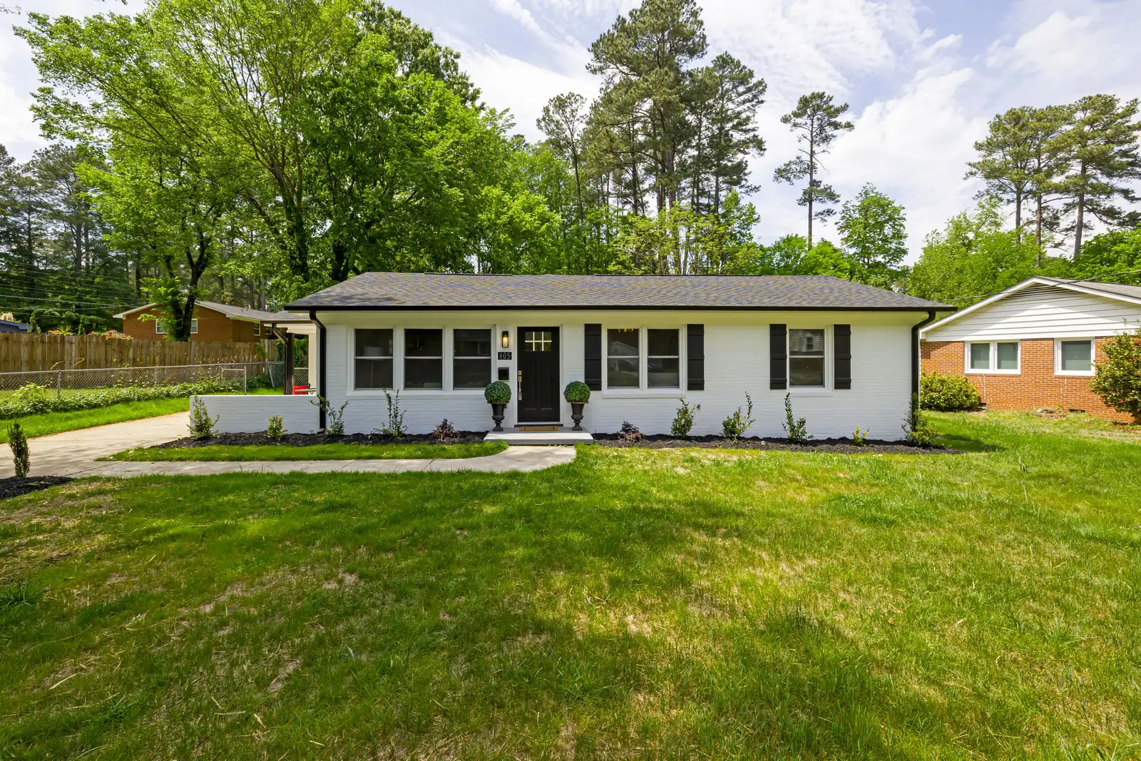 Single story white brick ranch home with a dark roof and a green front lawn