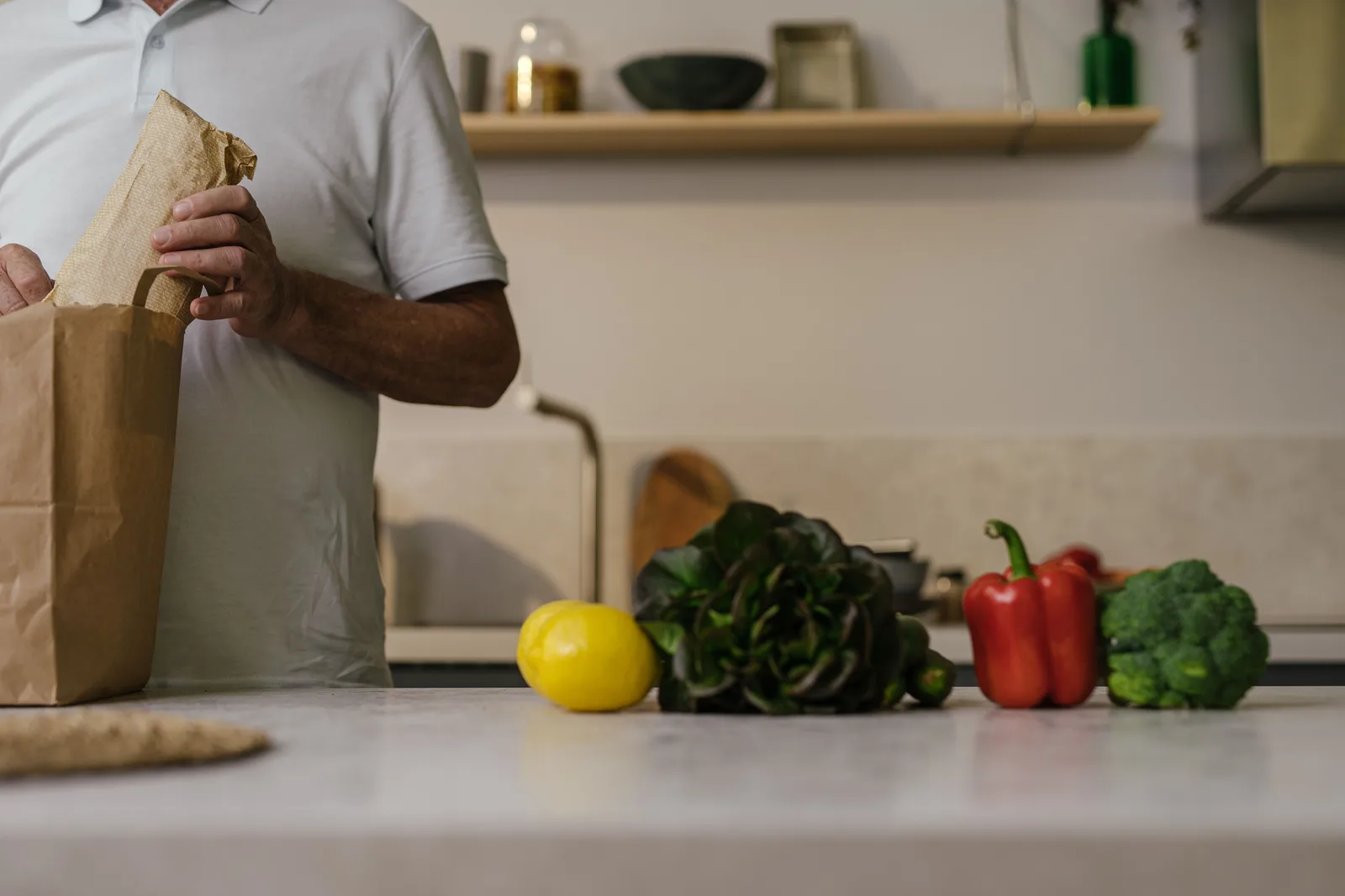 A person unpacking a paper grocery bag of fresh vegetables onto a kitchen counter