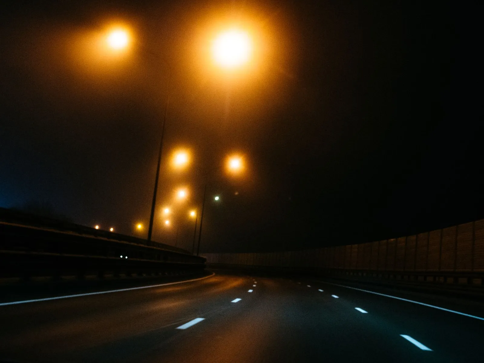 Empty asphalt highway curving away under orange streetlights at night