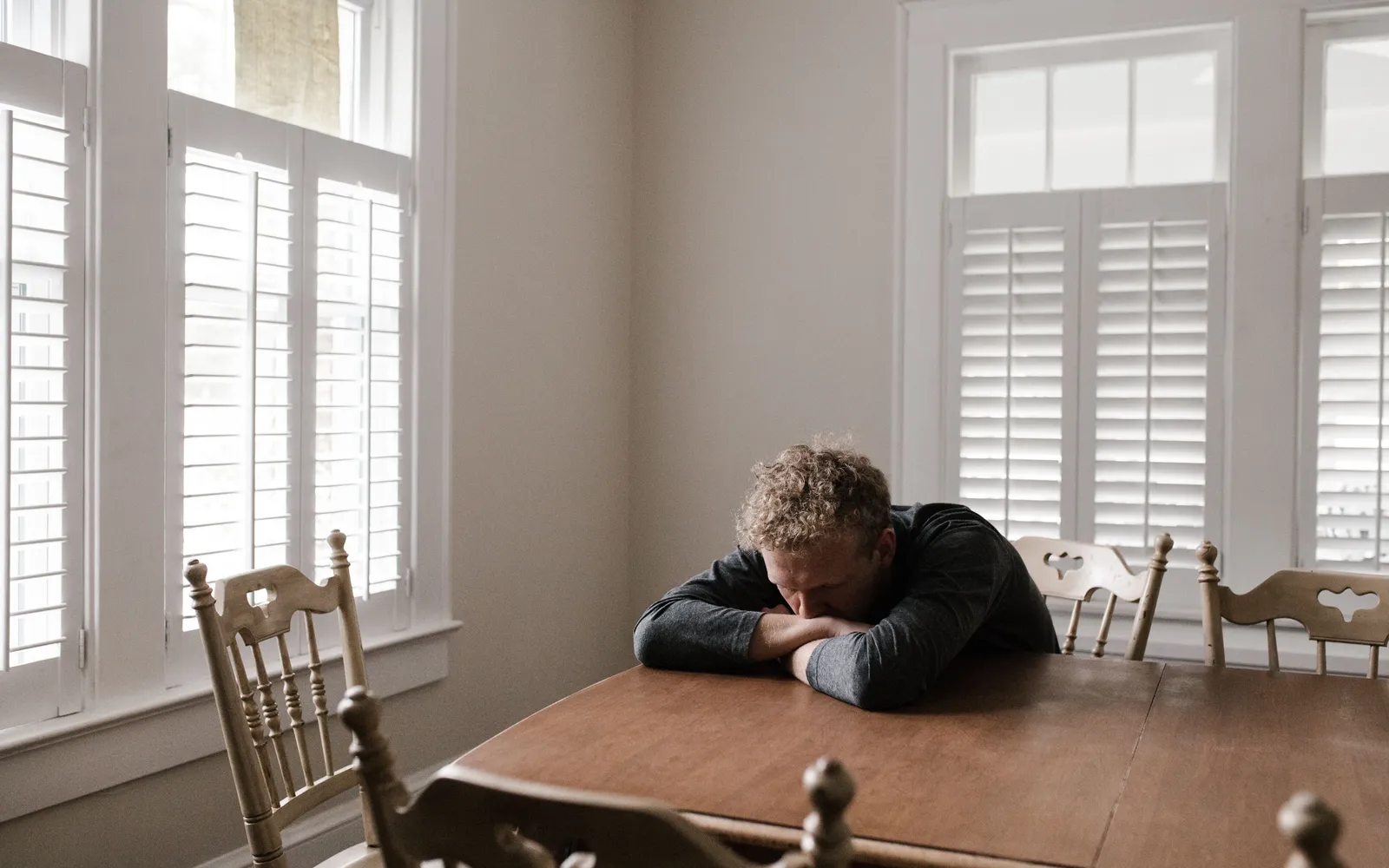 A man resting his head on his arms at a dining table in a bright room