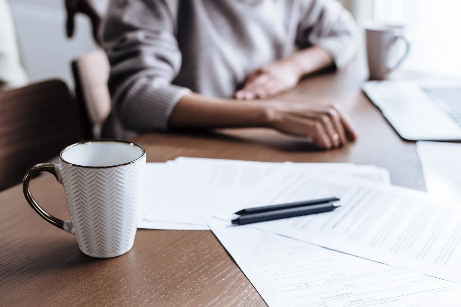 Someone going over paperwork and a laptop at a table with a coffee mug