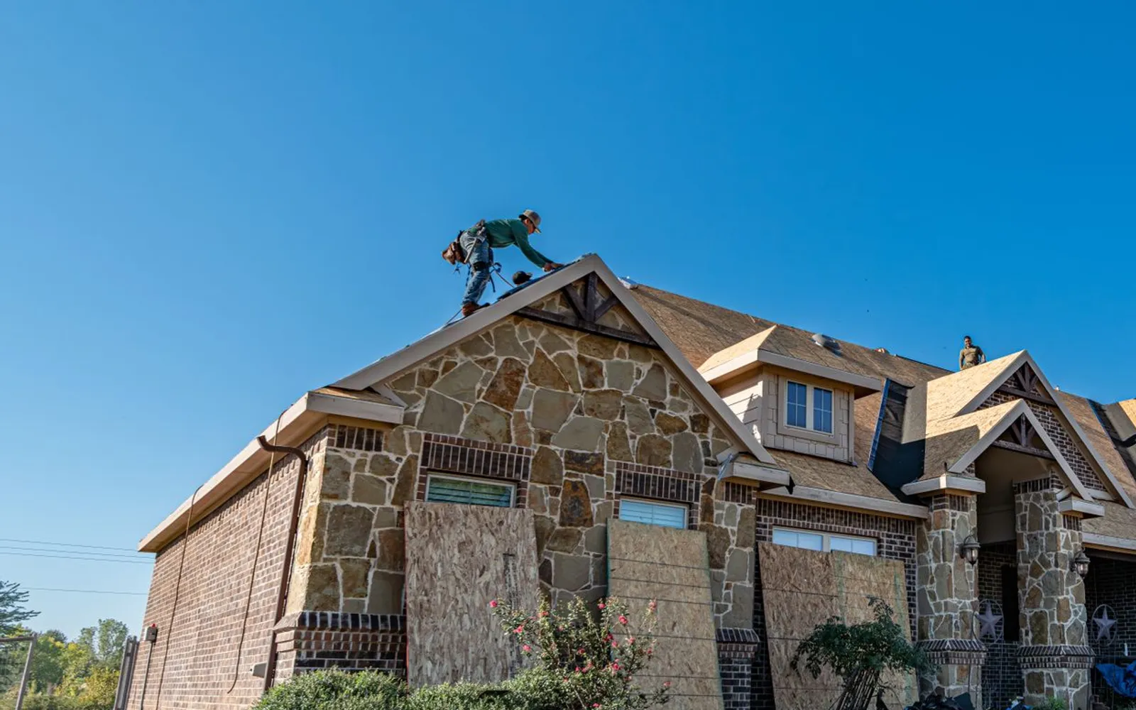 Crew replacing the roof on a brick and stone Texas house under a clear blue sky