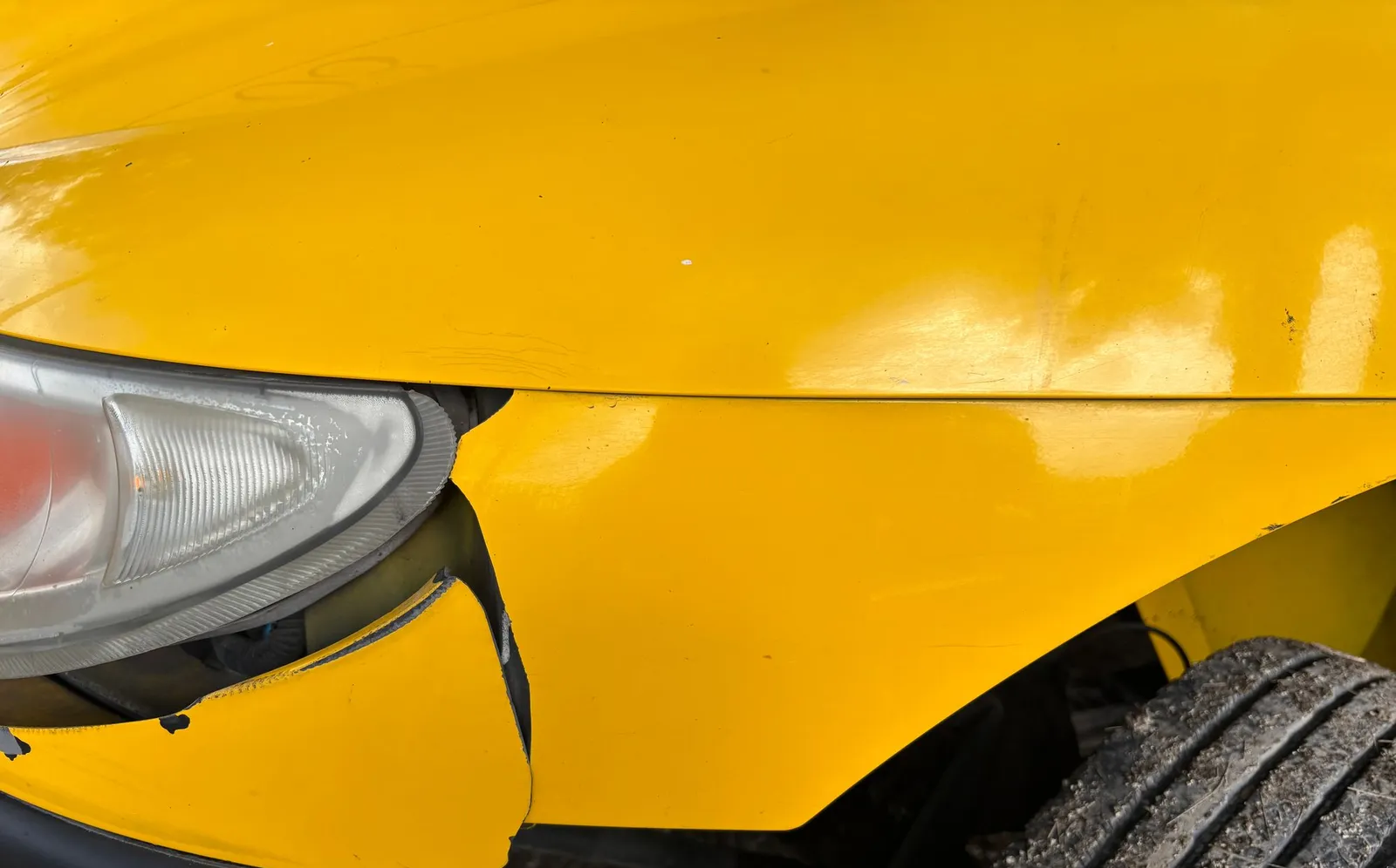 Close-up of a damaged front bumper and headlight on a yellow car
