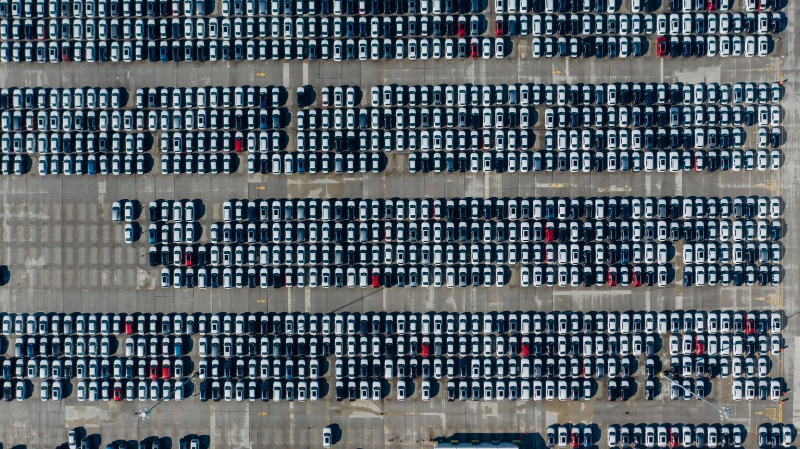 Overhead aerial view of hundreds of cars parked in neat rows at a vehicle storage lot