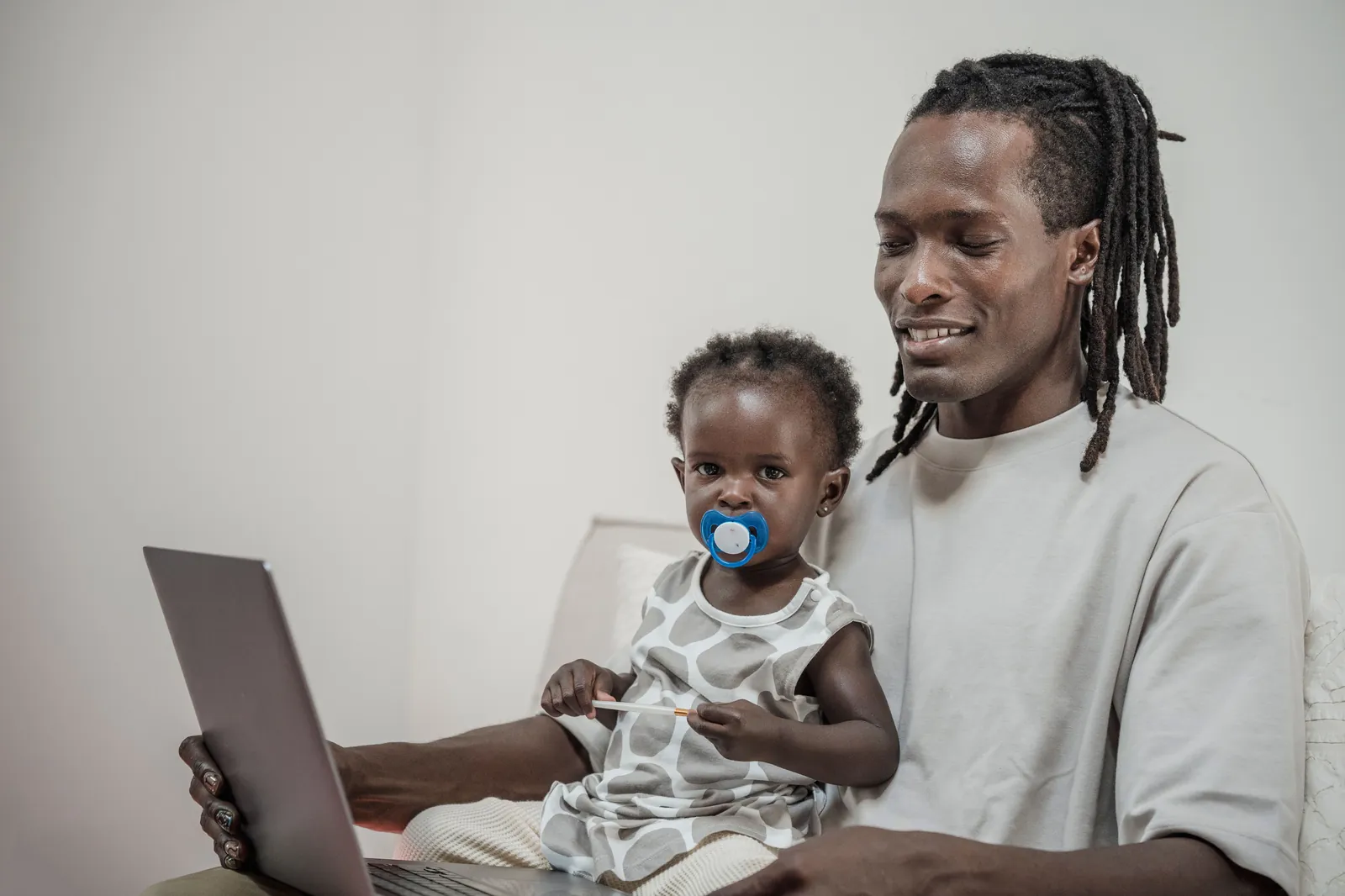 A father sitting at home with his infant daughter, checking a laptop screen together