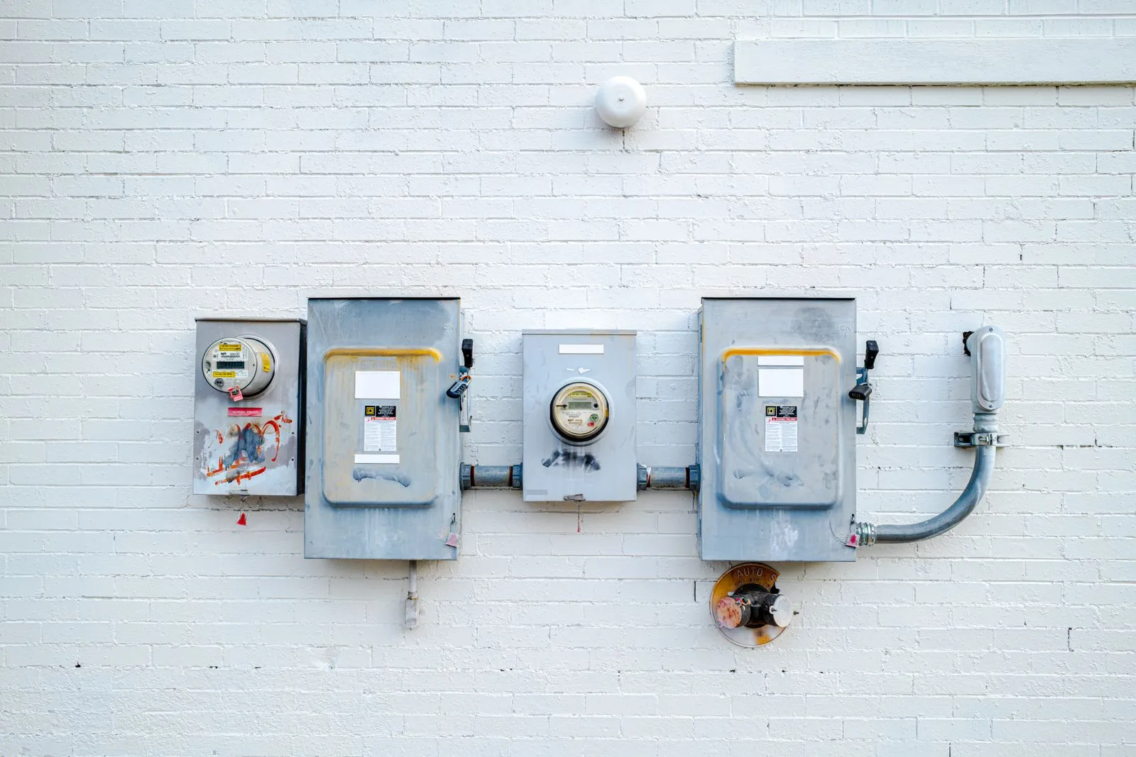 Row of electrical boxes and power meters mounted on a white brick wall