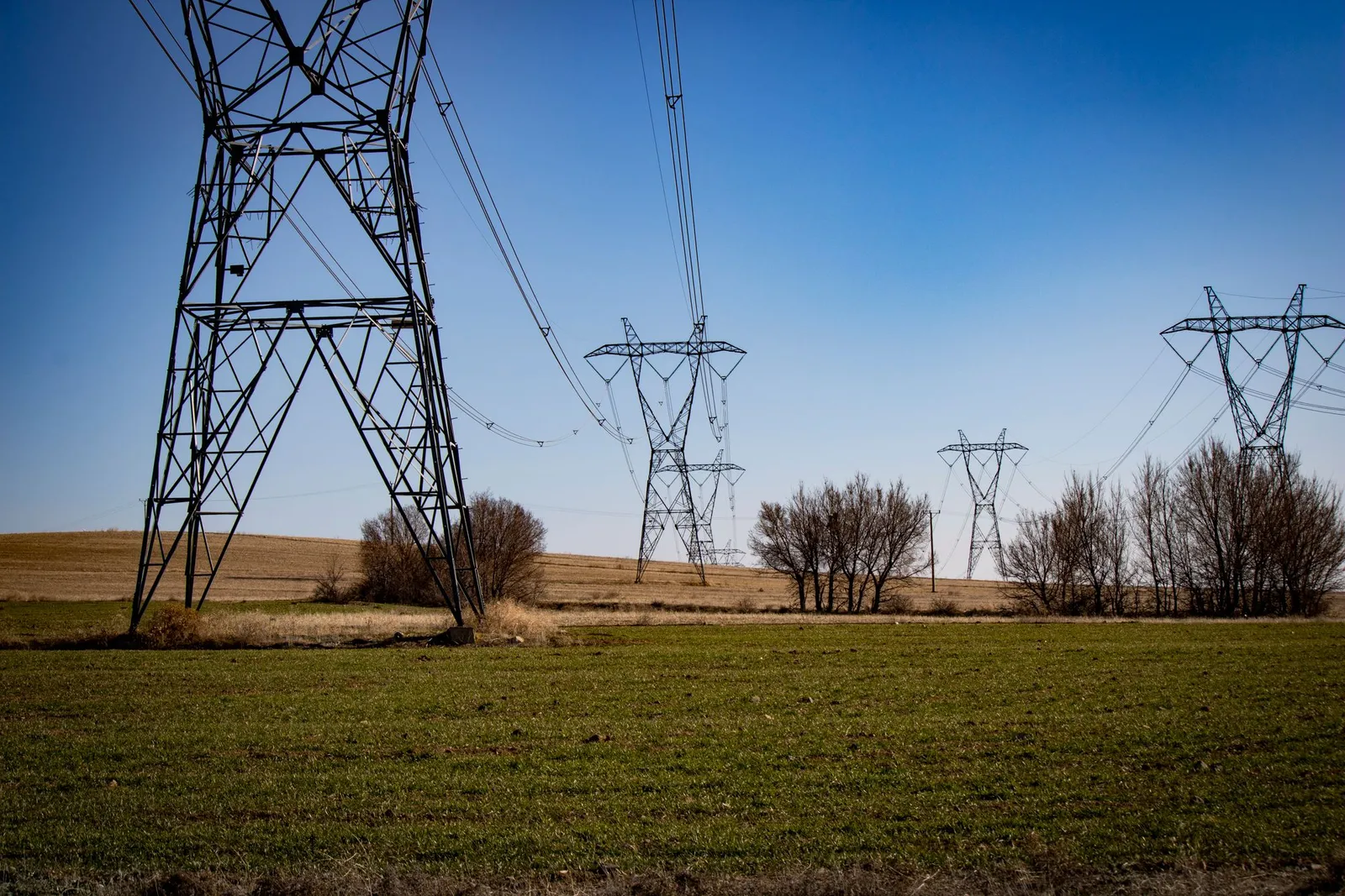 High-voltage transmission towers crossing a green field under a clear blue sky