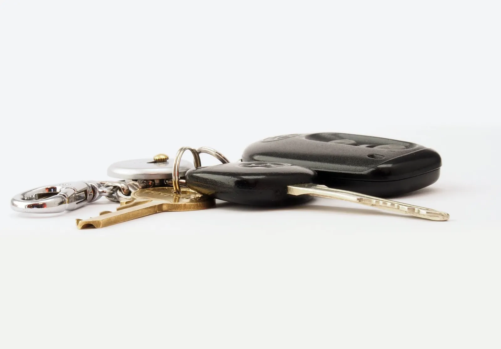 Set of car keys and two black key fobs resting on a plain white surface