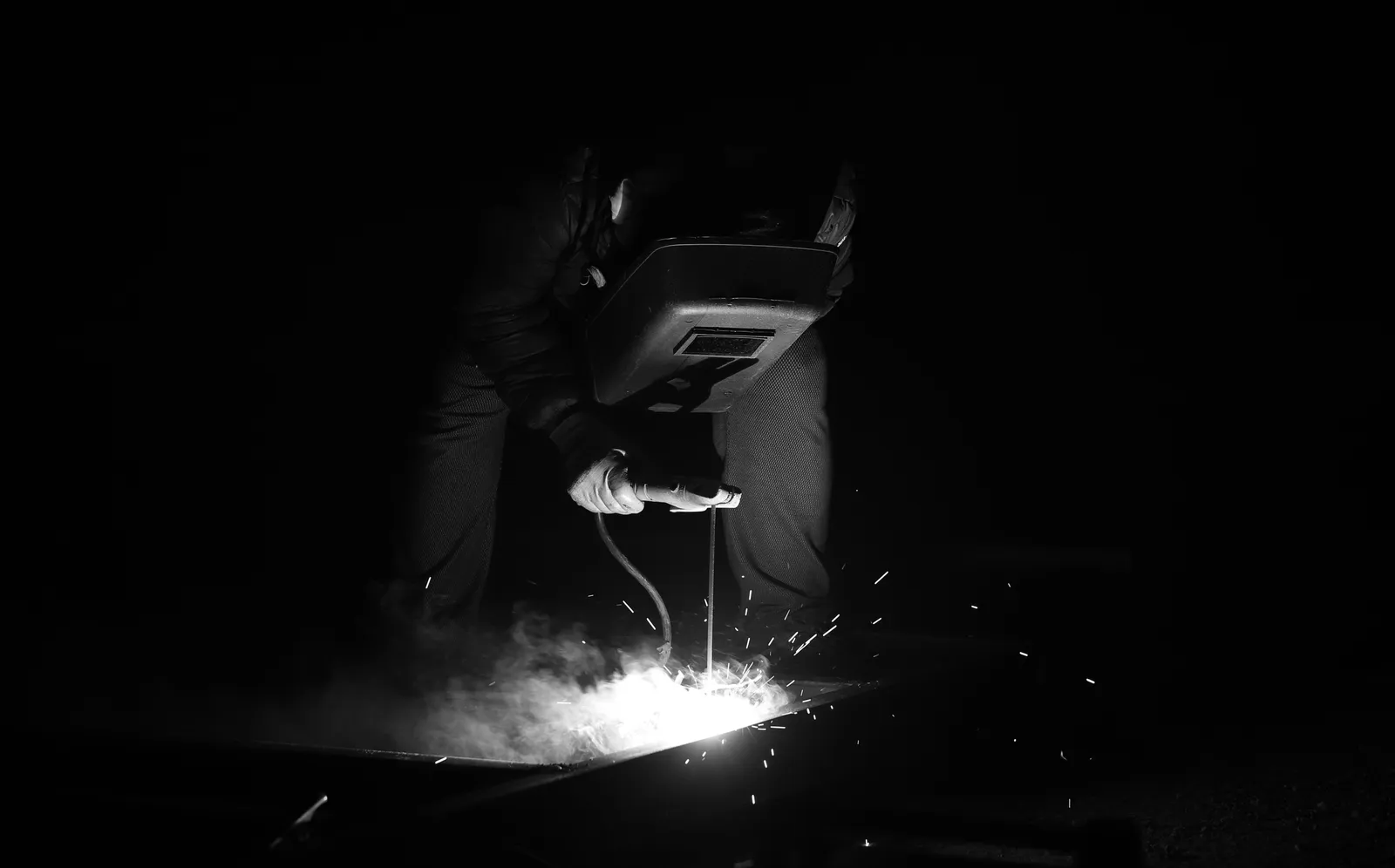 A welder in a dark workshop working on a metal sheet with sparks flying