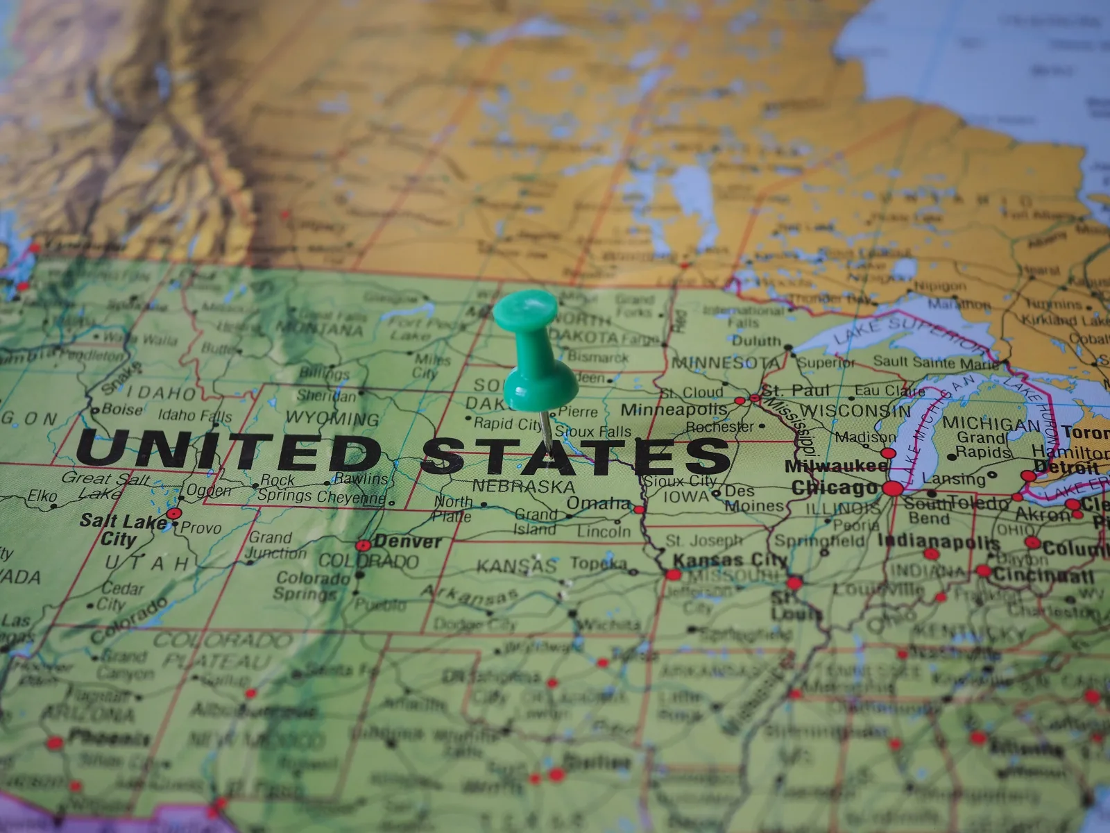 A green push pin stuck into a printed map of the United States near the center of the country