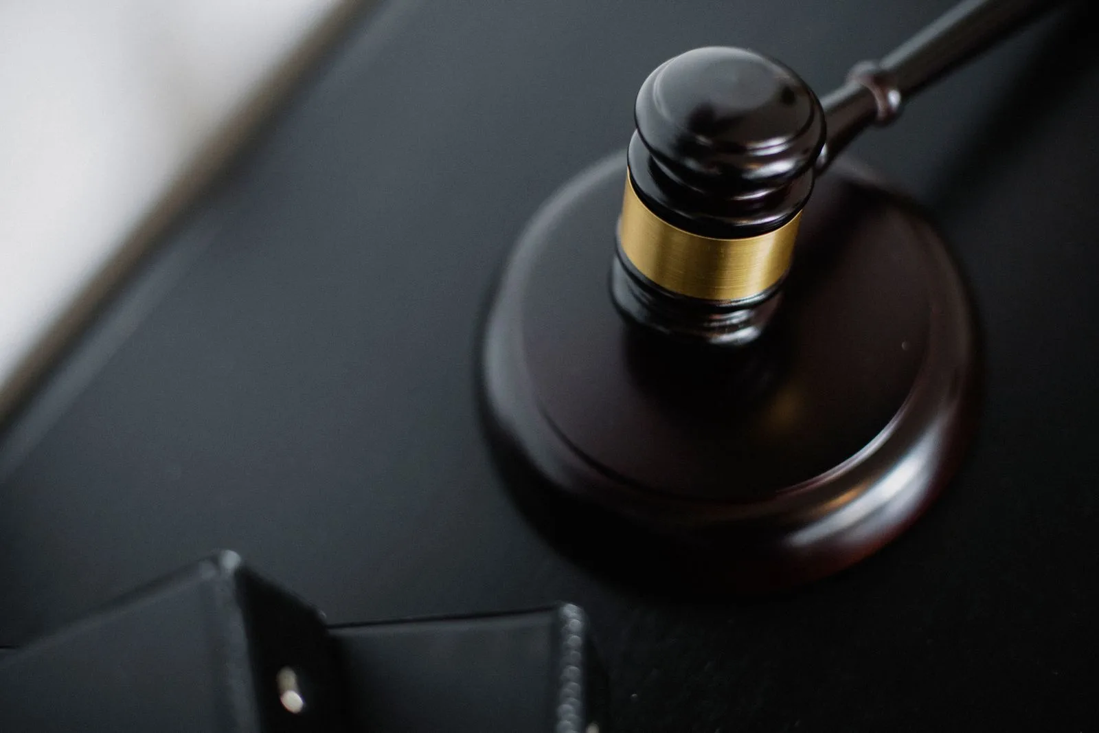 A wooden gavel with a brass band resting on its sound block on a dark desk, seen from above