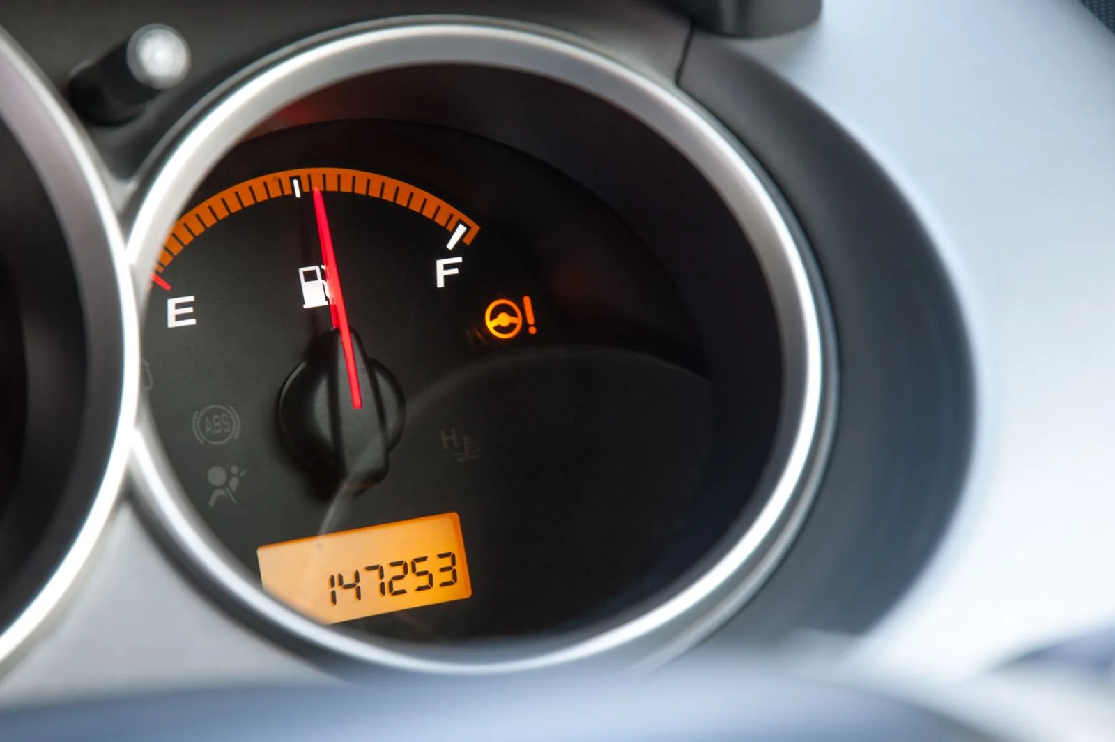 A close-up of a car fuel gauge with an amber odometer readout showing just over 147,000 miles