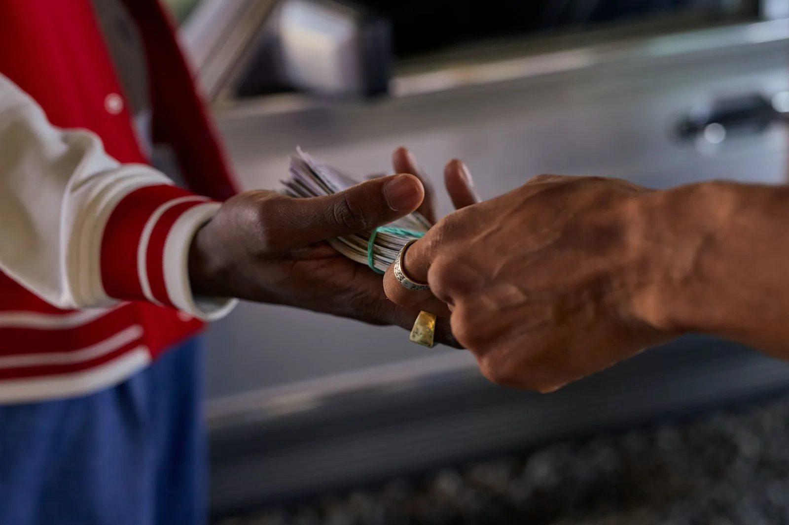 Two hands passing a rubber-banded bundle of cash beside the door of a parked car