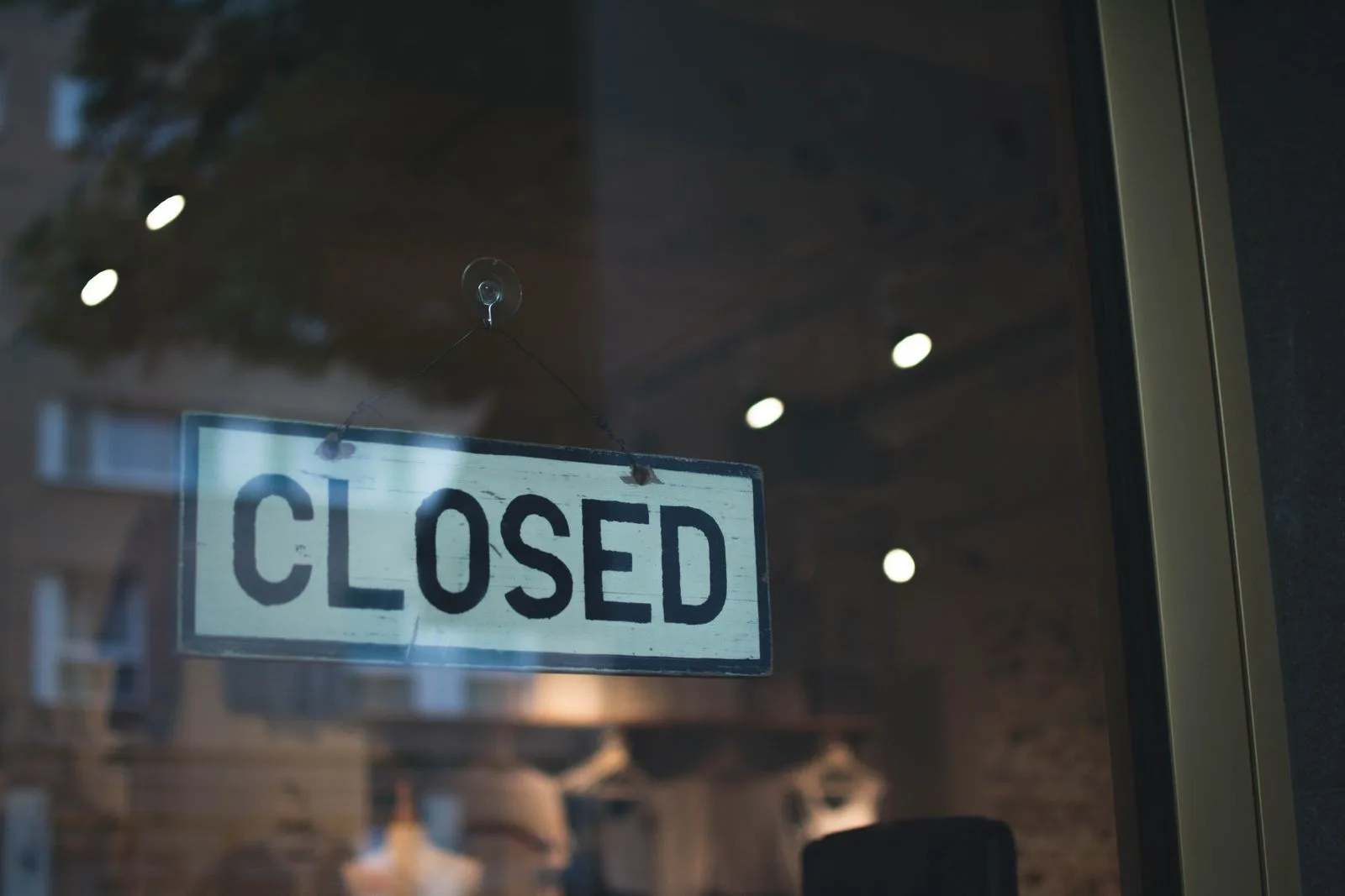 A hand-lettered CLOSED sign hanging by a wire on the inside of a dark shop door