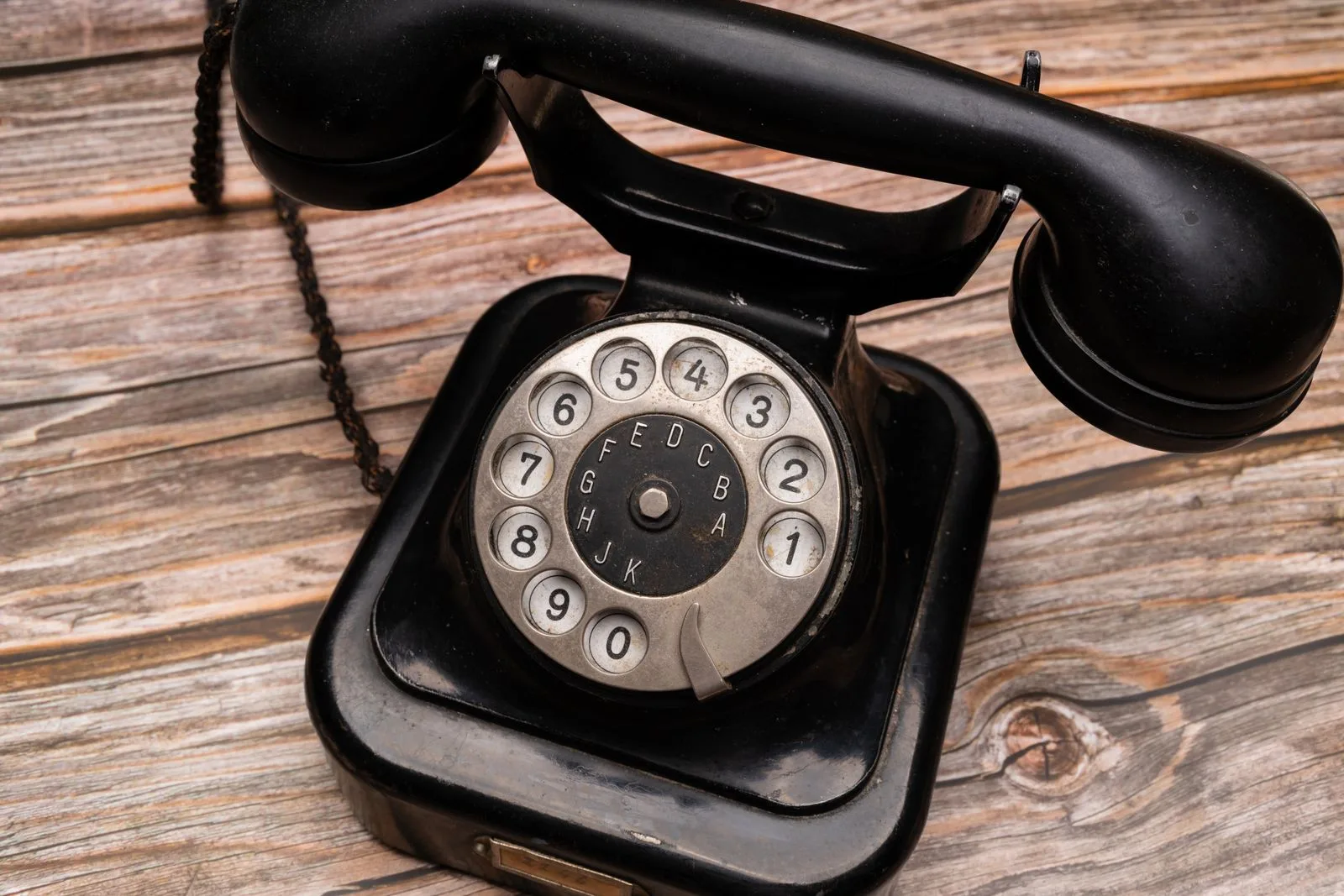 An old black rotary telephone with a chrome dial sitting on weathered wooden boards