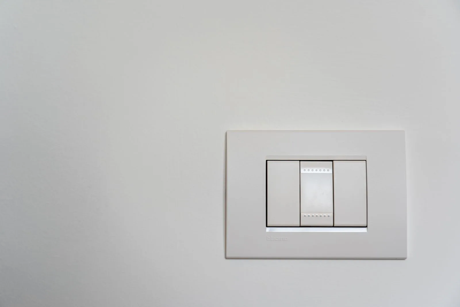 A plain white light switch on a bare white wall