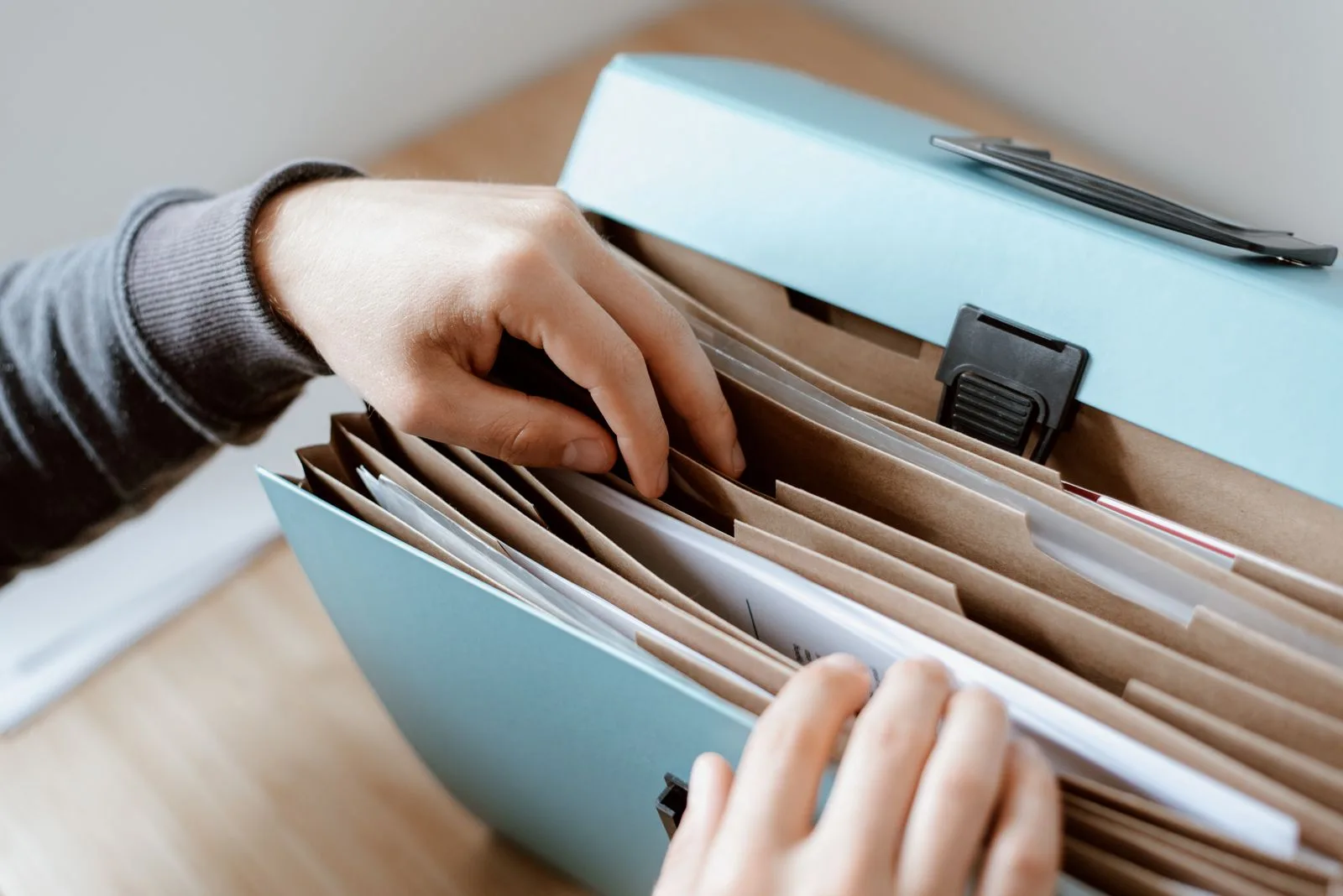 A pair of hands searching through the kraft dividers of an expanding document file on a light wood table